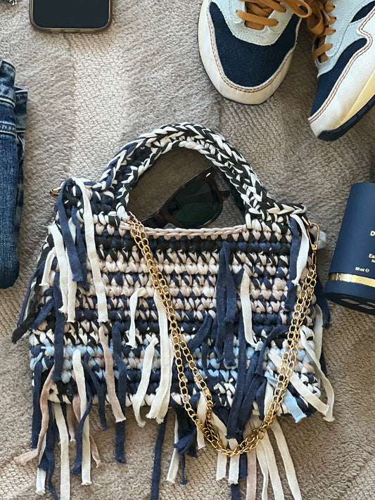 This glam showstopper handbag is interwoven with navy, cream, and beige eco-conscious yarns and it’s finished with free-spirited fringe and a luxe gold chain.